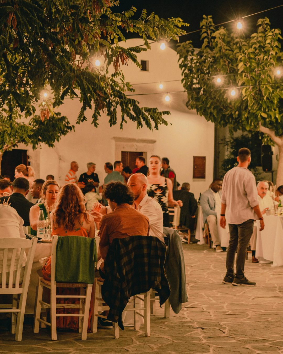 Guests seated at long outdoor dinner tables under string lights