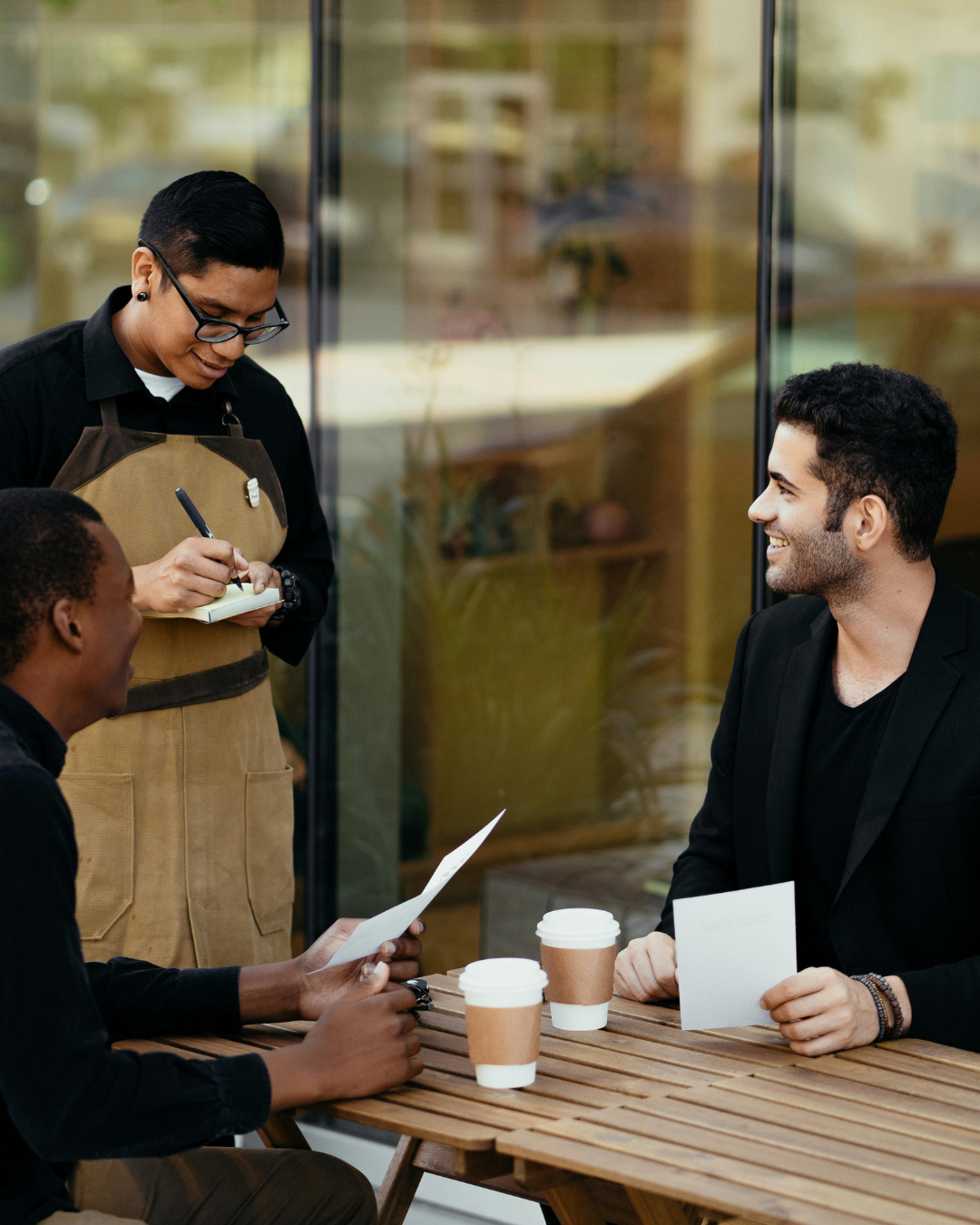 Server writing an order while two guests sit at a table with coffee
