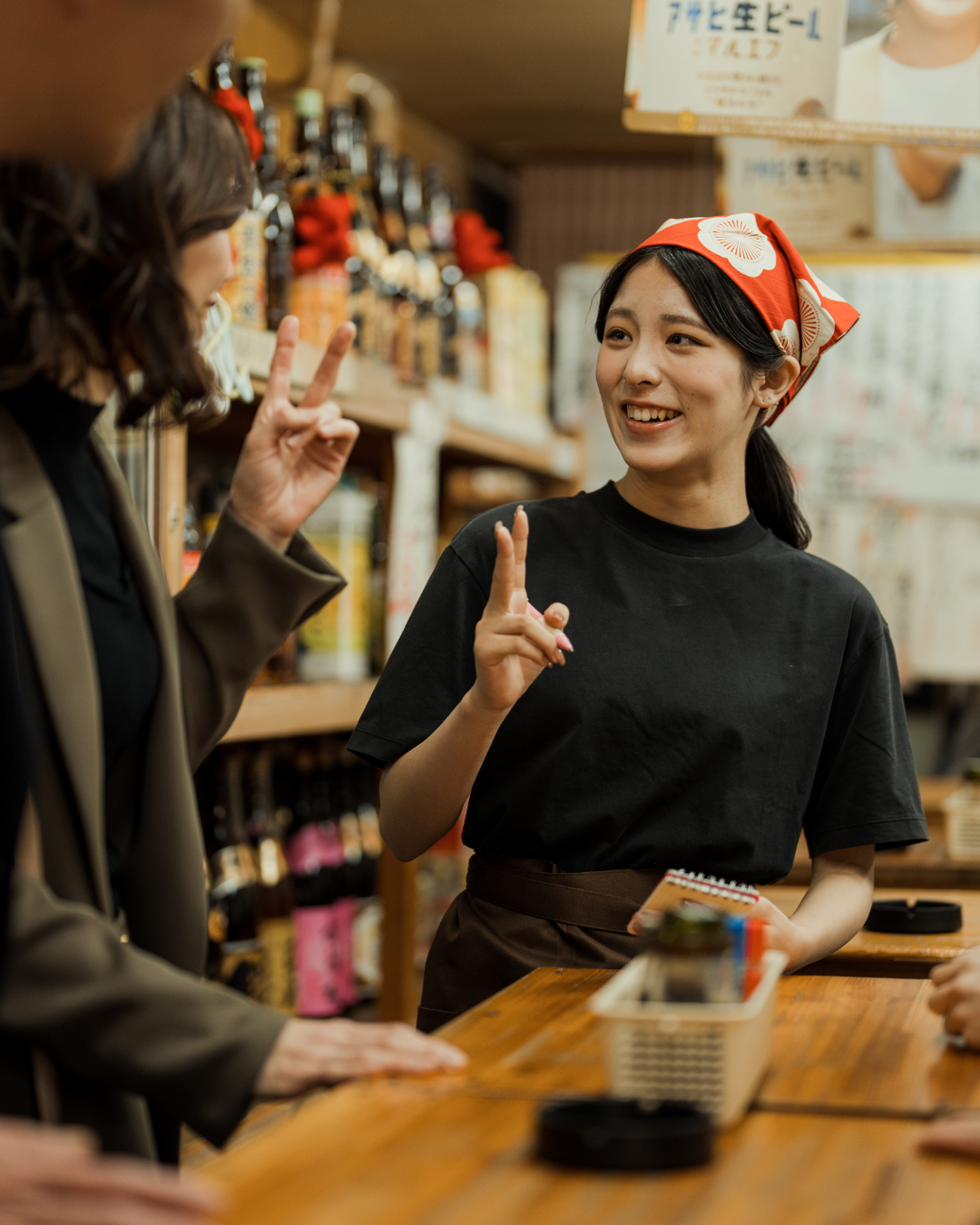 Smiling team member in a red bandana behind the counter holding up two fingers